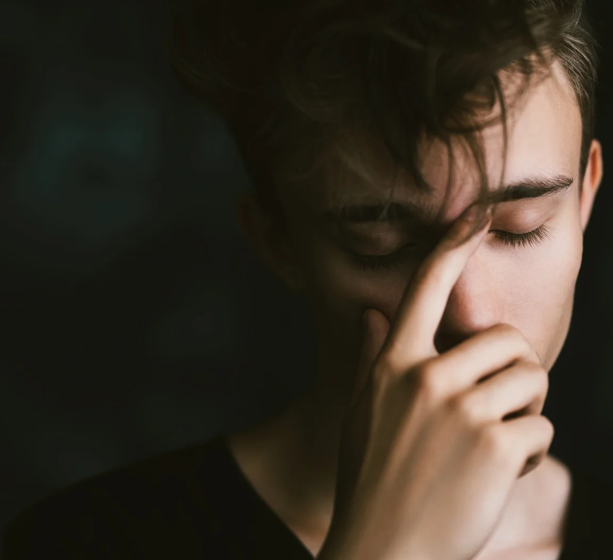 Young man with eyes closed, rubbing the bridge of his nose in a moment of stress or fatigue.